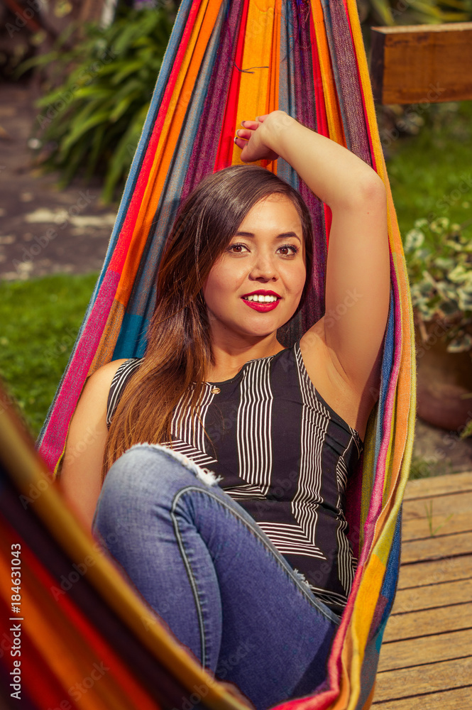 Close up of smiling young beautiful woman relaxing in a hammock with one arm behind of her head, in wooden nature background, vintage effect Close up of smiling young beautiful woman relaxing in a hammock with one arm behind of her head, in wooden nature background, vintage effect
