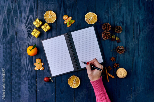 A girl with a red manicure in a knitted pink sweater writes a list of cases for the new year. A list of Christmas presents. Typical festive winter accessories, attributes, ornaments. photo