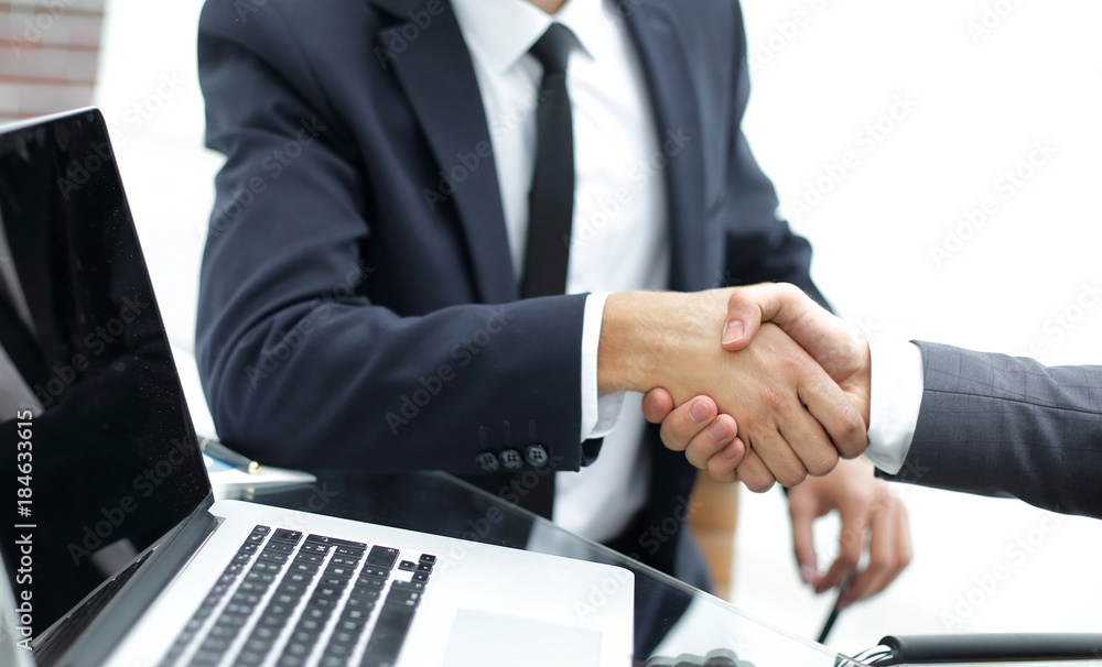 handshake business partners in front of the open laptop