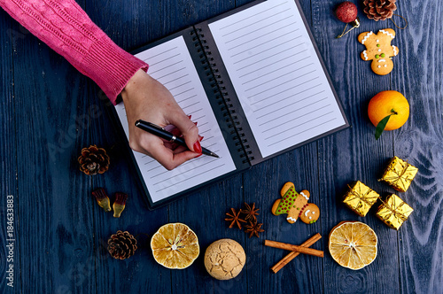 A girl with a red manicure in a knitted pink sweater writes a list of cases for the new year. A list of Christmas presents. Typical festive winter accessories, attributes, ornaments. photo