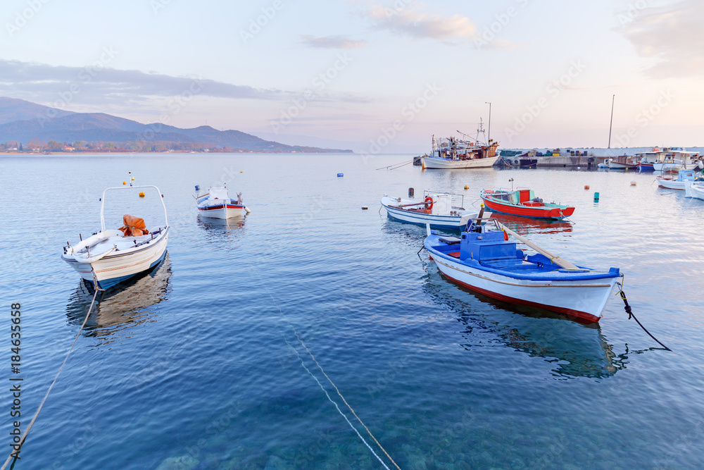 Greece, small port in coastal town Olimpiada (near Kavala) on Aegean sea. Dawn scenery of seafront. Fishing boats anchored to quay, beautiful morning landscape.