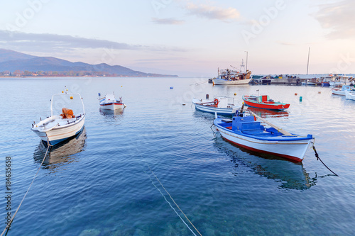 Greece  small port in coastal town Olimpiada  near Kavala  on Aegean sea. Dawn scenery of seafront. Fishing boats anchored to quay  beautiful morning landscape.