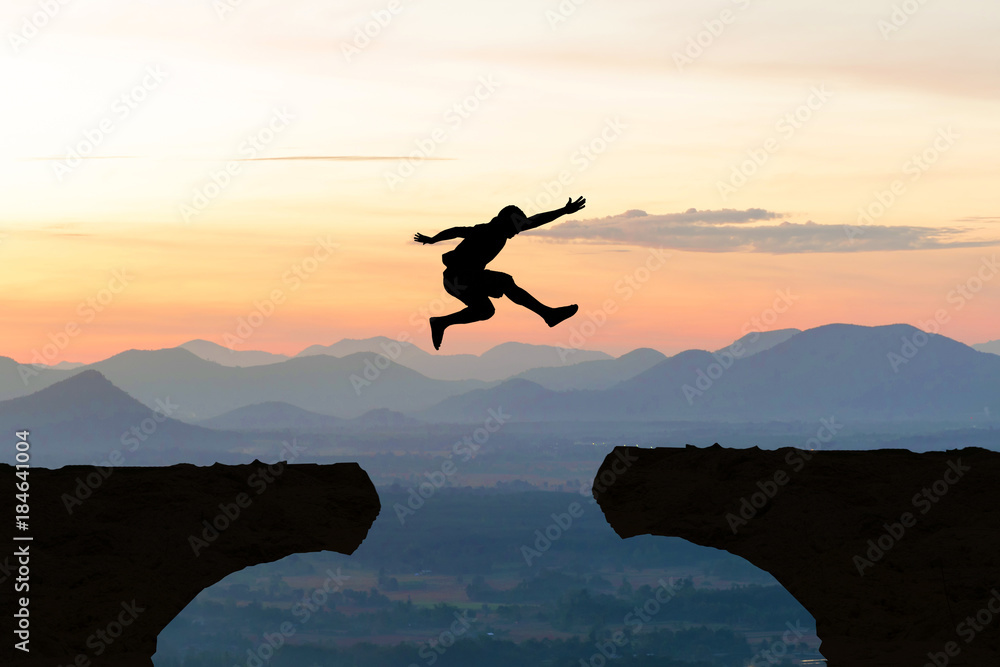 Man jump Mountain cliff sun light over silhouette