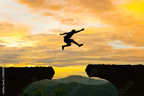 Man jump Mountain cliff sun light over silhouette