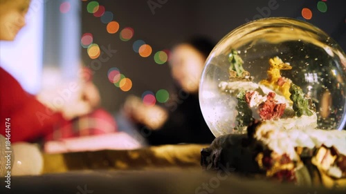 clouseup magic globe with snow and santa, on background blurred figure mother and daughter on the bed and garland in bokeh photo