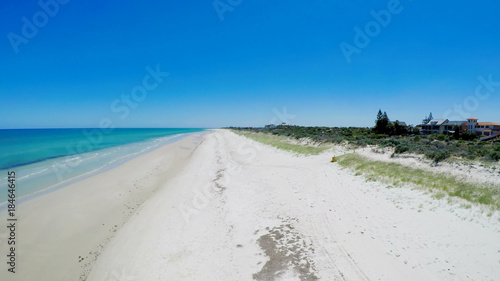 Drone aerial view of wide open white sandy beach, taken at Tennyson, South Australia with nearby luxury two story homes overlooking the coast.