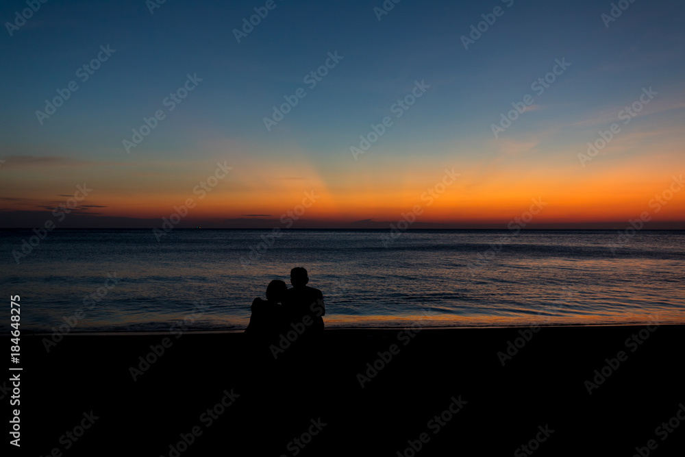 Male silhouette woman sitting hugging at the seaside with twilight