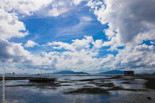 figures bamboo house and small ships in sibaltan beachin low tide time in El Nido, Phillipines, Palawan province with cloudly sky and mountain on foreground