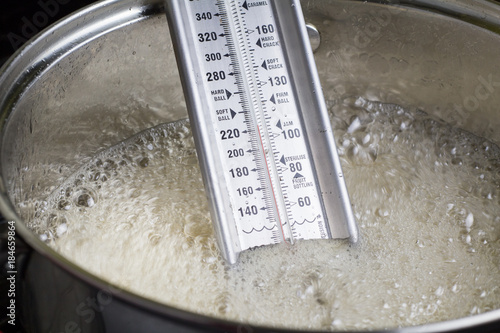 Candy thermometer close up in boiling liquid in metal pot