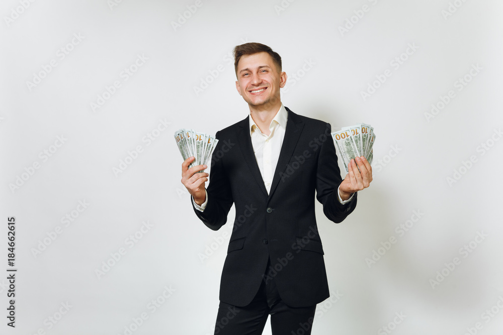 Young successful handsome rich business man in black suit holding wad of cash dollars isolated on white background for advertising. Concept of money, achievement, career and wealth in 25-30 years. Young successful handsome rich business man in black suit holding wad of cash dollars isolated on white background for advertising. Concept of money, achievement, career and wealth in 25-30 years.