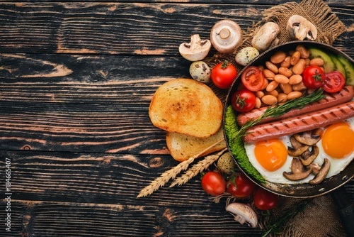 English breakfast - fried egg, beans, tomatoes, mushrooms, bacon and toast. Top view. On a wooden background.