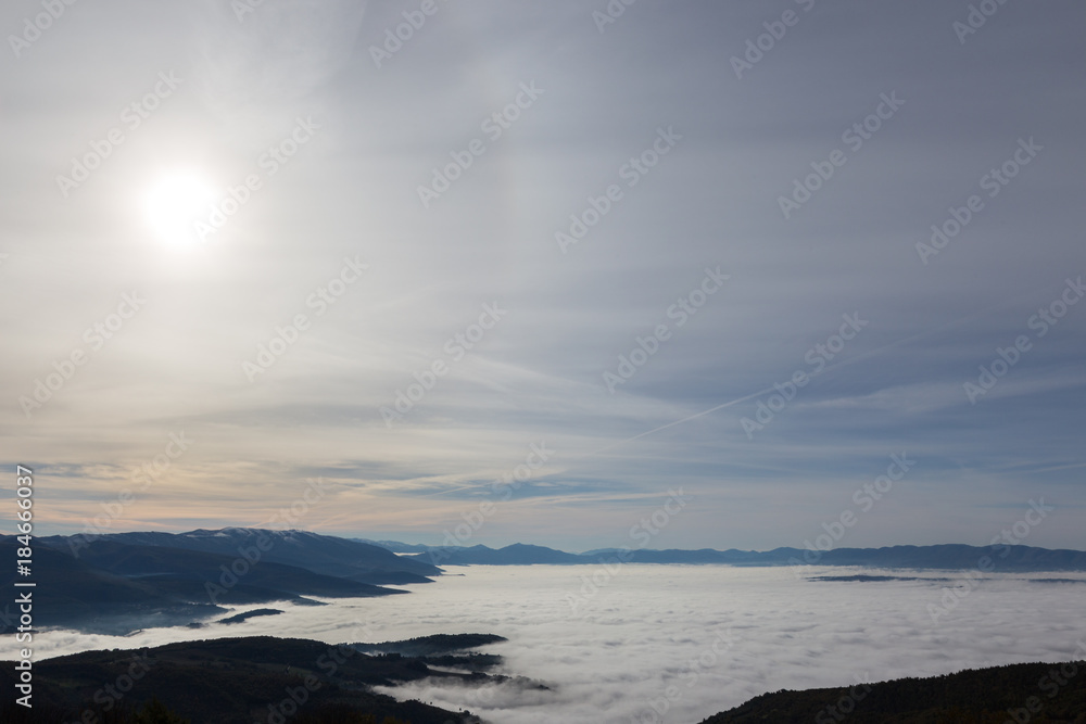 Fog filling Umbria valley, with layers of mountains and hills and various shades of blue, and sun filtered through the clouds