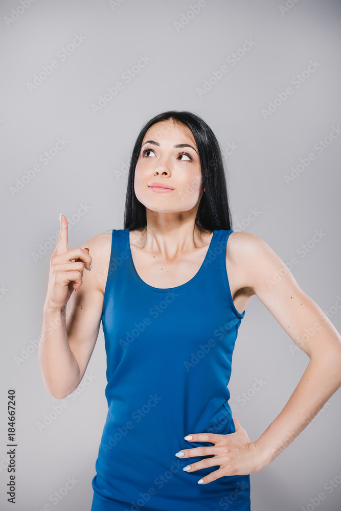 young thoughtfull teen with long brunette hair in blue dress, holding finger up in photostudio on gray background young thoughtfull teen with long brunette hair in blue dress, holding finger up in photostudio on gray background