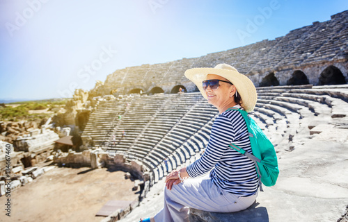 Mature beautiful woman traveler, sits on the steps of the amphitheater in admiring the view. Travel to Greece and Turkey, the monuments of ancient architecture, active seniors
