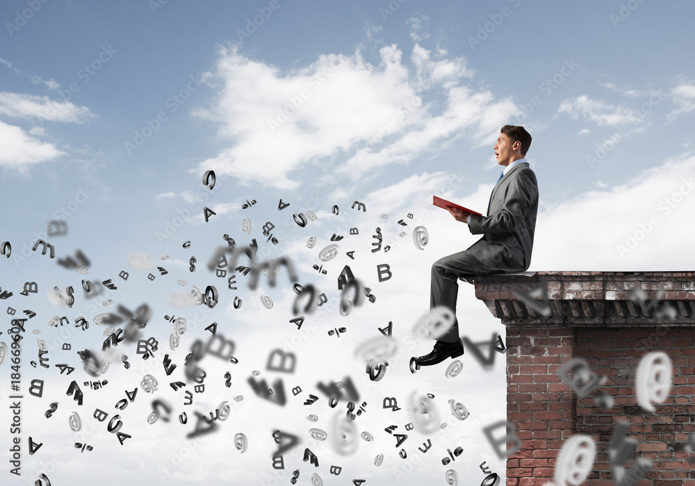 Man on roof edge reading book and symbols flying around Man on roof edge reading book and symbols flying around