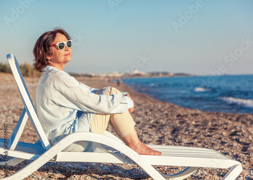 фотографія beautiful elderly woman sitting in a deckchair on the beach and admiring the sun
