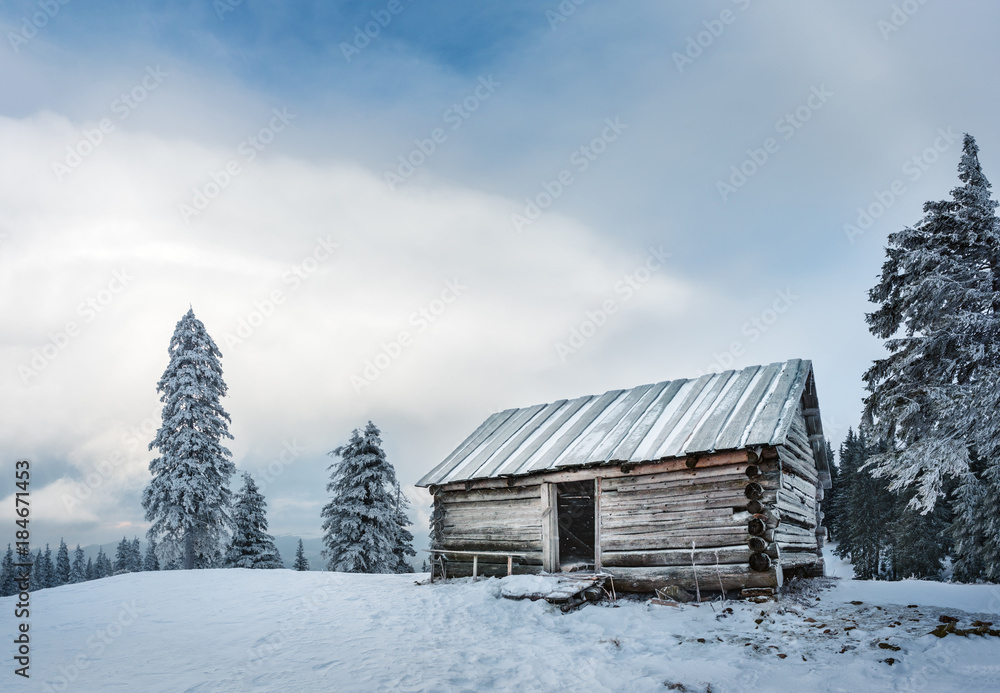 Lonely empty house on the mountain hill in winter. Mountain slope with fir trees covered with snow. Lonely empty house on the mountain hill in winter. Mountain slope with fir trees covered with snow.