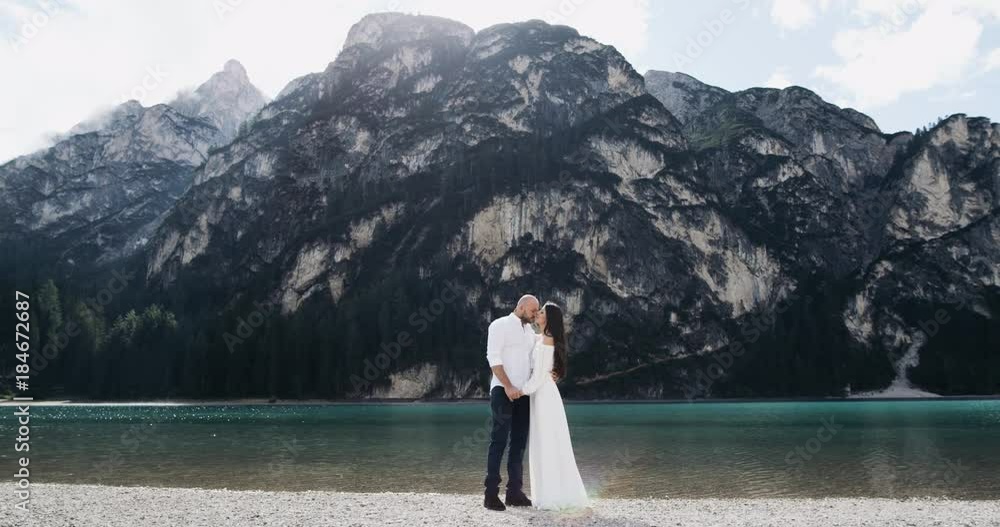 Young beautiful couple kissing in the middle of a amazing landscape with mountains and lake. 4k Young beautiful couple kissing in the middle of a amazing landscape with mountains and lake. 4k