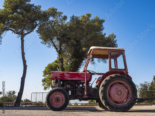 Old pink tractor with oblezajushhej paint on a background of blue sky and trees, sunny day