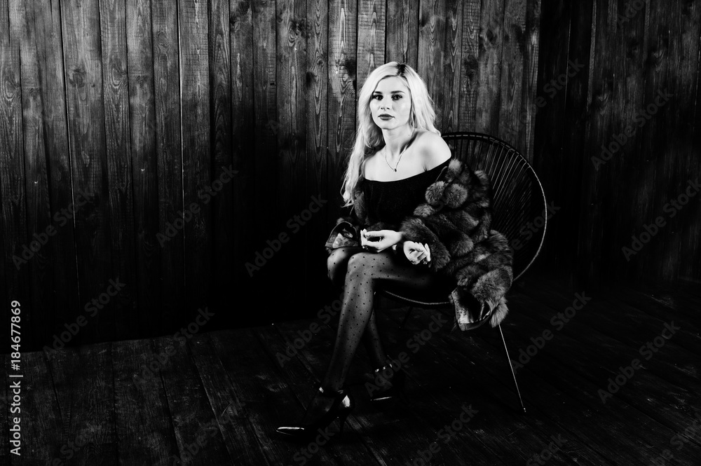 Elegante blonde girl wear on fur coat sitting on chair at studio against wooden background. Elegante blonde girl wear on fur coat sitting on chair at studio against wooden background.