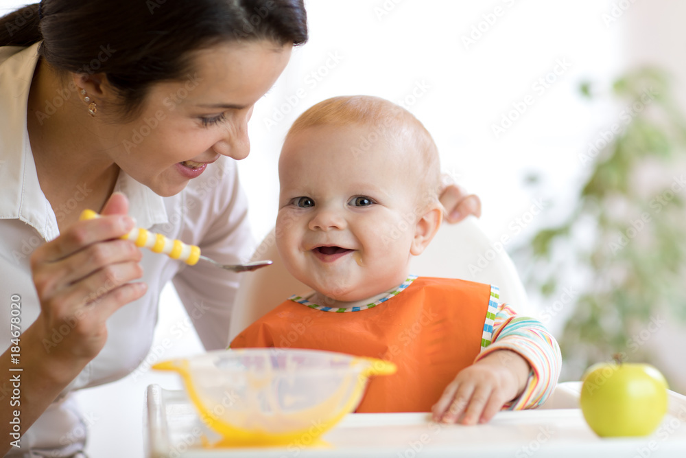 Mother feeding her baby with spoon. Mother giving healthy food to her adorable child at home Mother feeding her baby with spoon. Mother giving healthy food to her adorable child at home