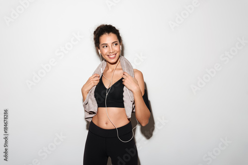 Smiling curly brunette fitness woman with towel listening music