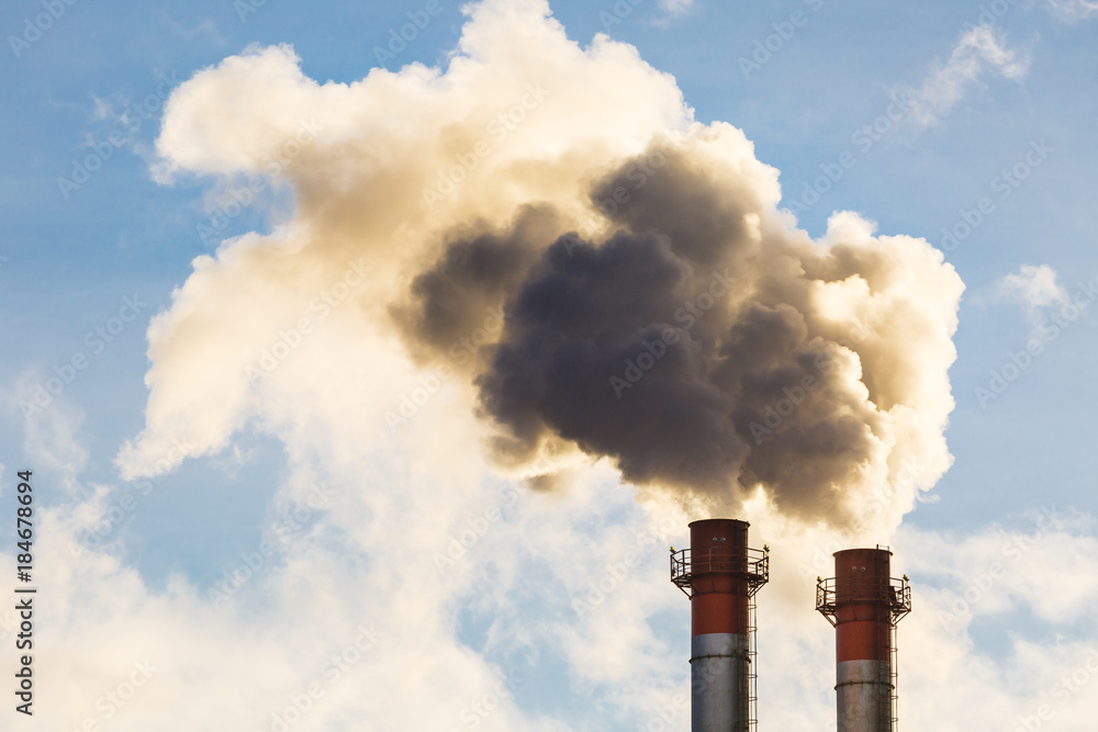 Stream of dark smoke from the chimney of factory in the industrial district