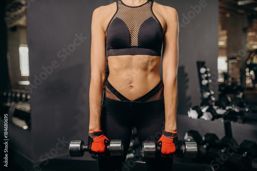 Muscular body of a young gymnastic woman, abs close up. Woman's abs. In hands dumbbells
