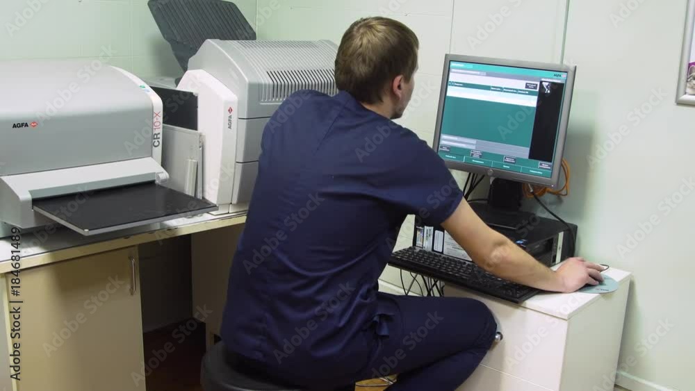 Doctor behind the monitor in the X-ray room looks at the image of the patient. Doctor behind the monitor in the X-ray room looks at the image of the patient.