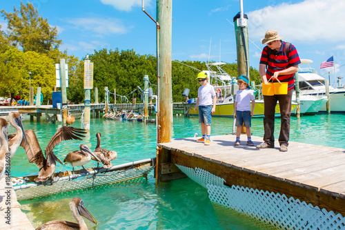 father and two little kid boys feeding fishes and pelicans