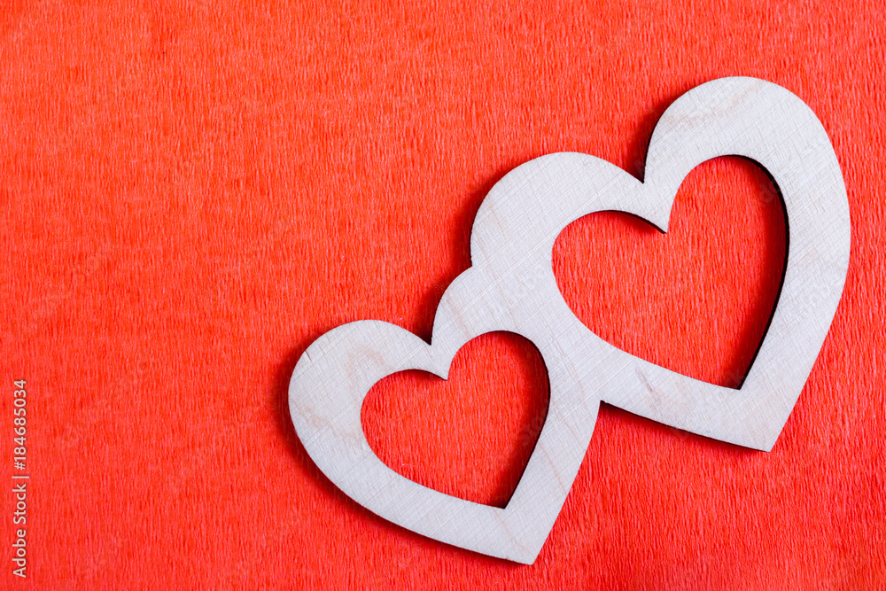 Two carved wooden hearts are lying diagonally on red textured paper background and copy space.