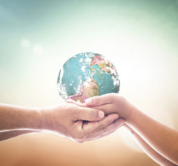 Earth Day concept with adult and child hands holding globe for future generation and environmental protection in soft nature background with light bokeh and copy space for text