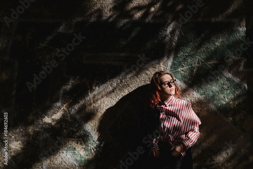 Portrait of young beautiful girl wearing stylish shirt, black skinny jeans, glasses. Girl have shinny long red hair. Female fashion concept