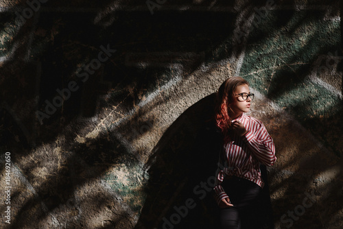 Portrait of young beautiful girl wearing stylish shirt, black skinny jeans, glasses. Girl have shinny long red hair. Female fashion concept
