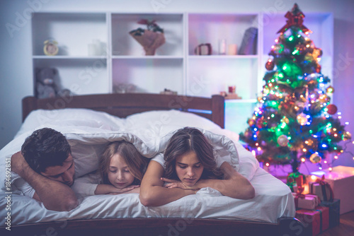 The family sleeping on the bed near the christmas tree. evening night time