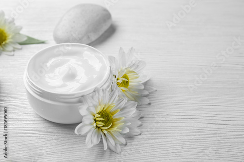 Jar of body cream and flowers on light background