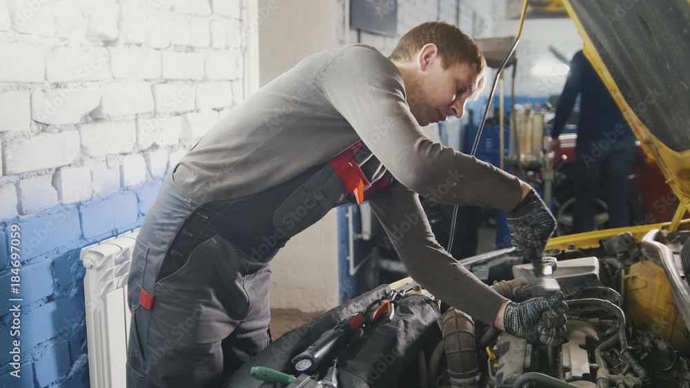 Mechanic in car repairing service - diagnostics in engine compartment