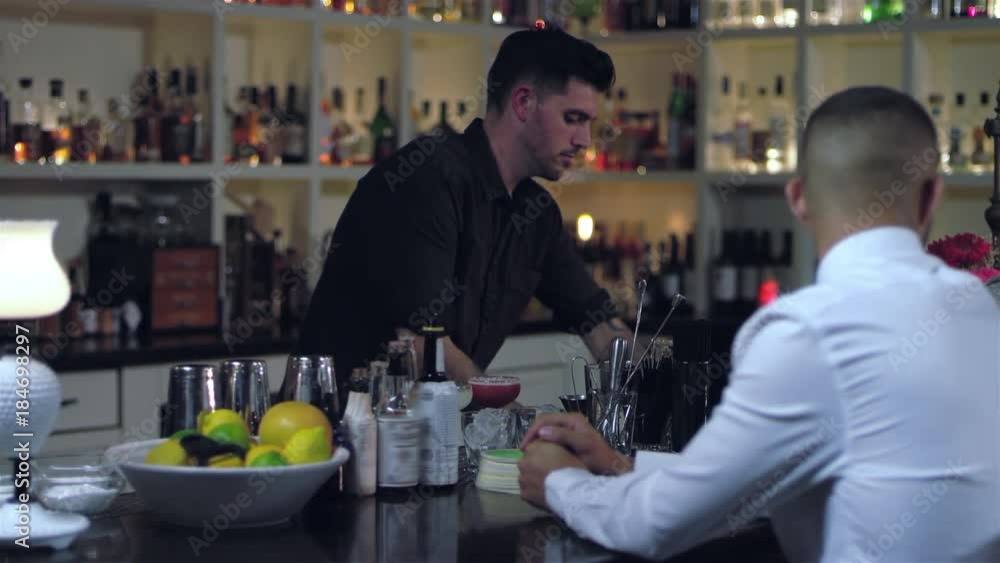 Young attractive bartender looks focused as he prepares alcoholic drinks for his costumers at a bar Young attractive bartender looks focused as he prepares alcoholic drinks for his costumers at a bar