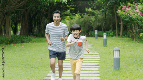 Chinese father & son smiling & running in park in summer