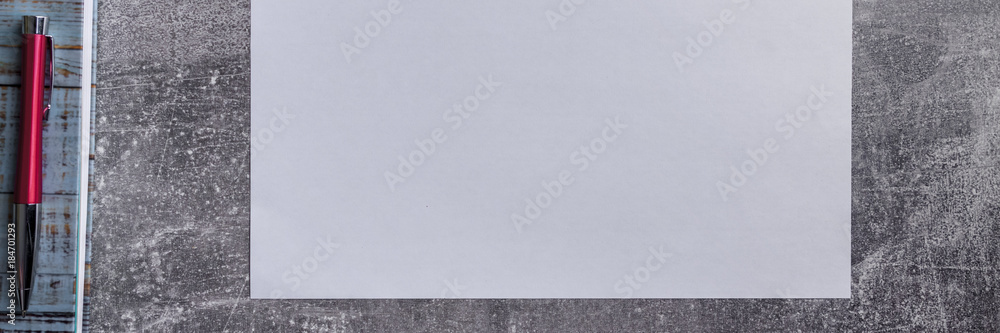 Panoramic concrete grey table top with a blank white sheet of paper, a blue circle notebook and a red elegant business pen Panoramic concrete grey table top with a blank white sheet of paper, a blue circle notebook and a red elegant business pen
