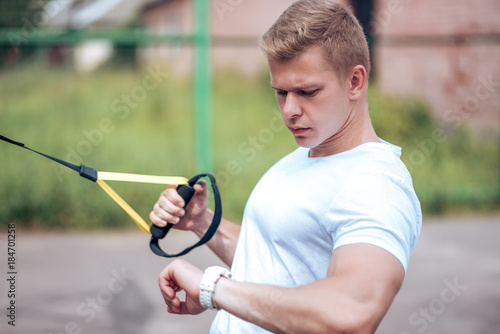 A male athlete goes in for sports in the open air. Muscular arms. Blonde in a white T-shirt. Lifestyle of the bodybuilder