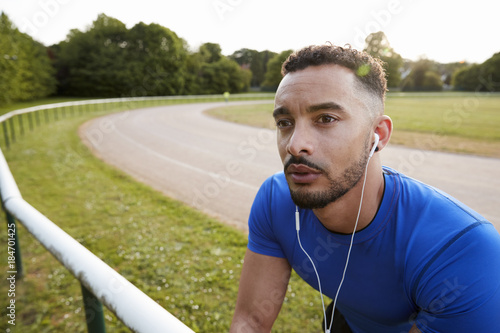 Male athlete wearing earphones at running track, close up