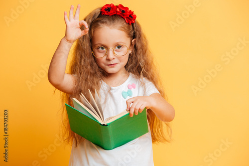 Little cute pretty girl reading book showing okay gesture.