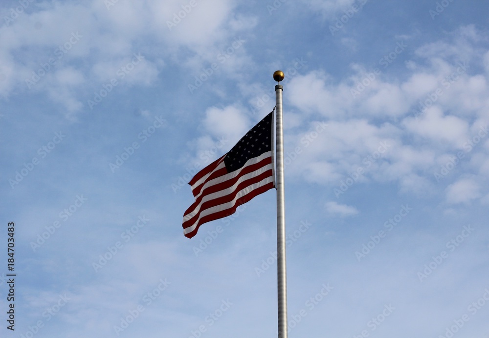 The USA flag blows in the wind with the clouds in the sky.