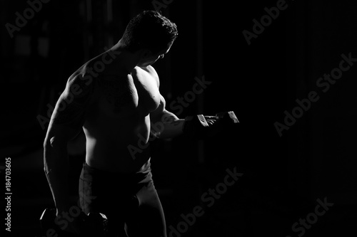 Handsome power athletic guy bodybuilder doing exercises with dumbbell. Fitness muscular body on dark background. black and white © Artem Zakharov
