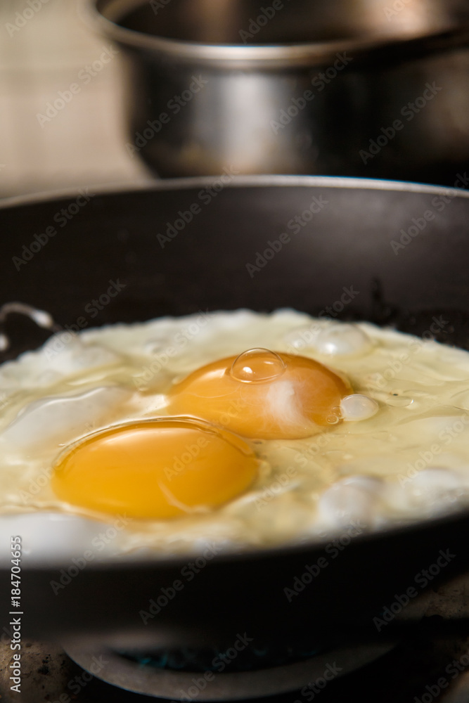 Two eggs frying in teflon skillet with defocused aluminum pan in background. Two eggs frying in teflon skillet with defocused aluminum pan in background.