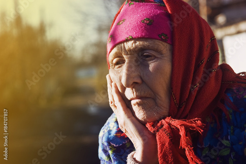 Sad, wrinkled face of the old mother standing beside the road