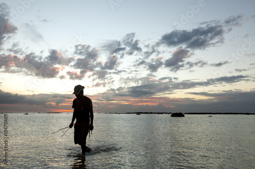 A fisherman catches a fish in the ocean at sunset.