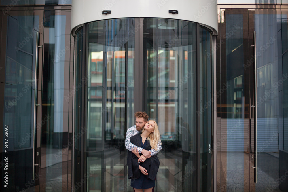 A man hugs a woman in the background of the glass building. A man hugs a woman in the background of the glass building.