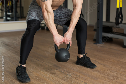 Beautiful man squats with kettlebell at the gym